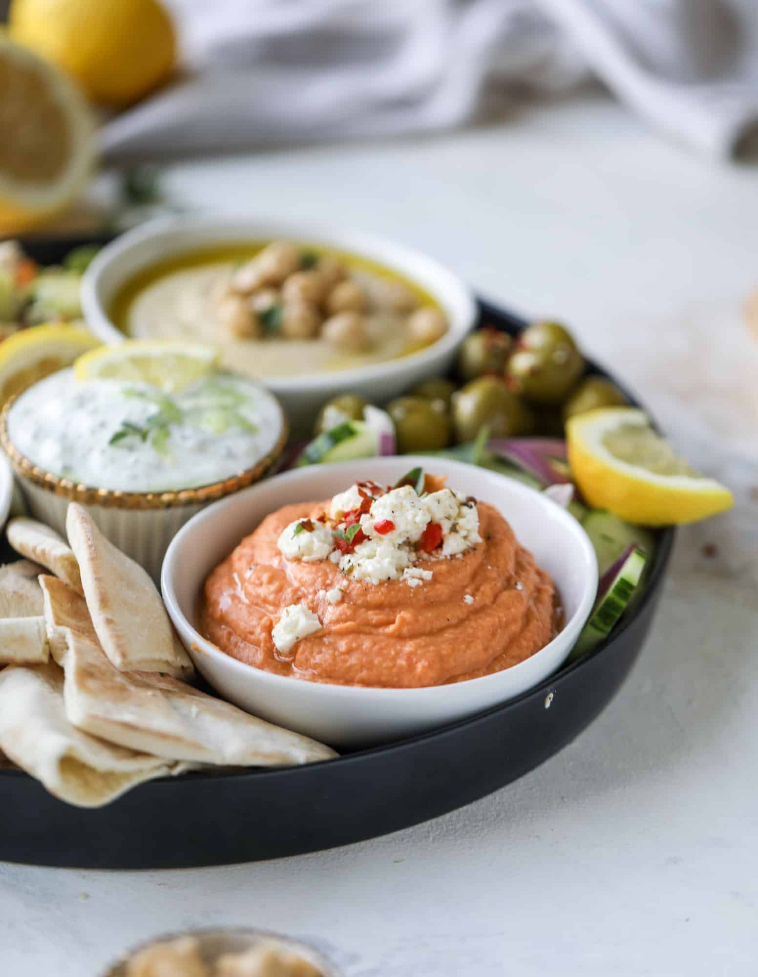 Here you can find out how to make the perfect hummus platter! This trio includes caramelized onion hummus, smoky black bean hummus and roasted red pepper white bean hummus, along with a couscous salad and quick tzatziki! I howsweeteats.com #hummus #platter #appetizer #snack #chickpeas #healthy #blackbeans #yogurt #tzatziki
