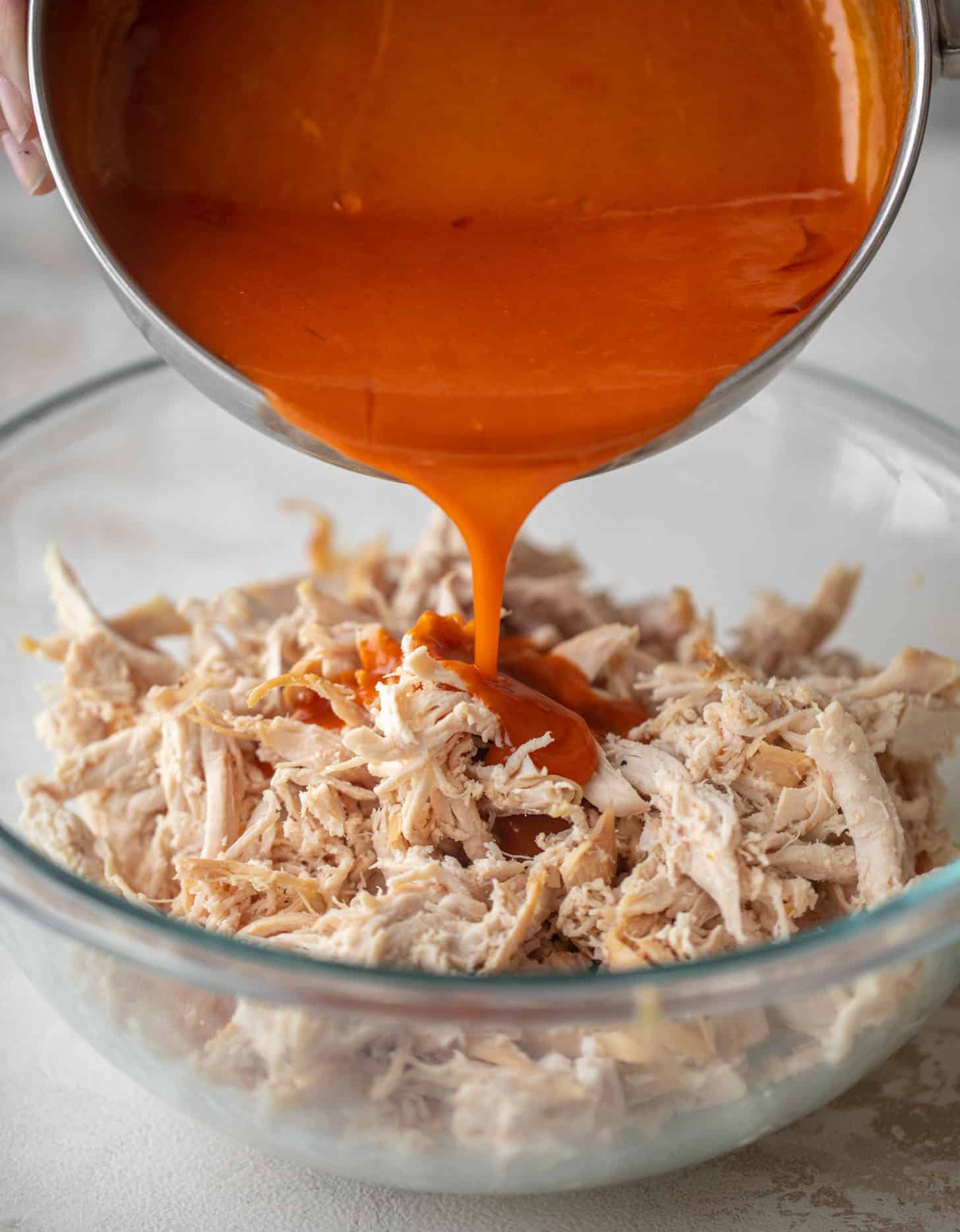 pouring buffalo wing sauce on shredded chicken